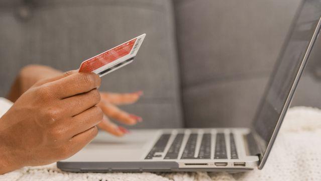 a person holding a credit card in front of their laptop